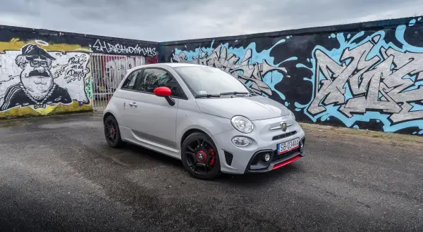 Szary Abarth 595 z czerwonymi akcentami na tle kolorowego graffiti.