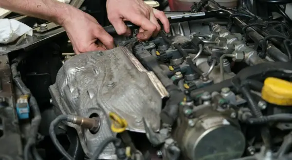 Mechanik pracuje przy silniku, sprawdzając czujnik położenia wałka rozrządu. Objawy jego awarii mogą być różne.