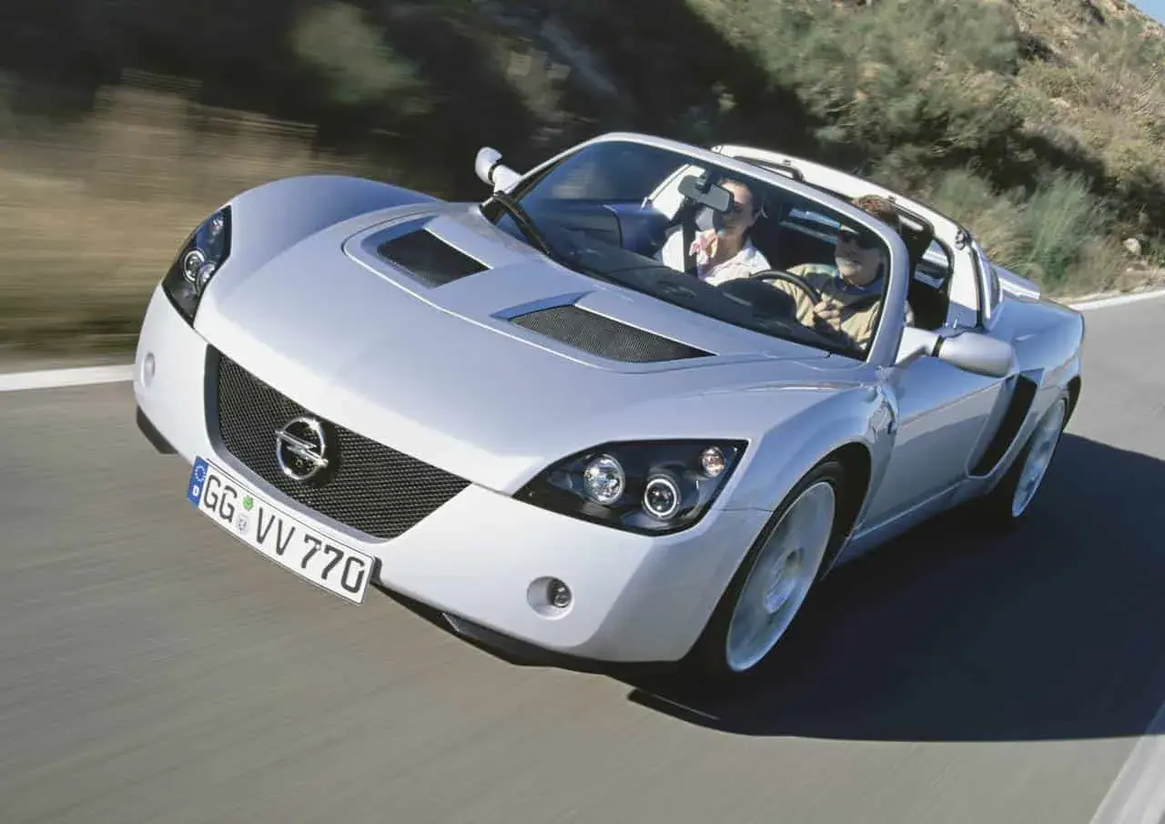 Srebrny Opel Speedster z parą na pokładzie mknie po krętej drodze.