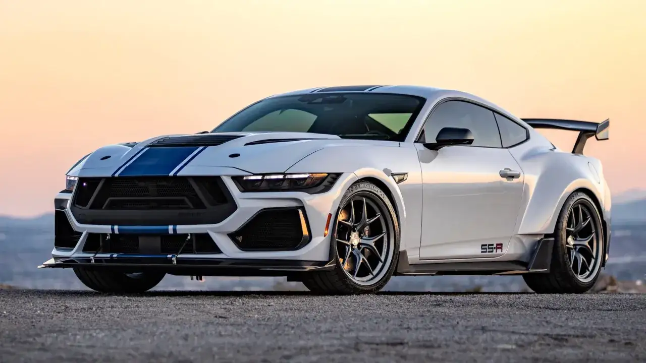 Biały Ford Shelby z niebieskimi pasami, szerokimi błotnikami i spoilerem, gotowy do podboju drogi.