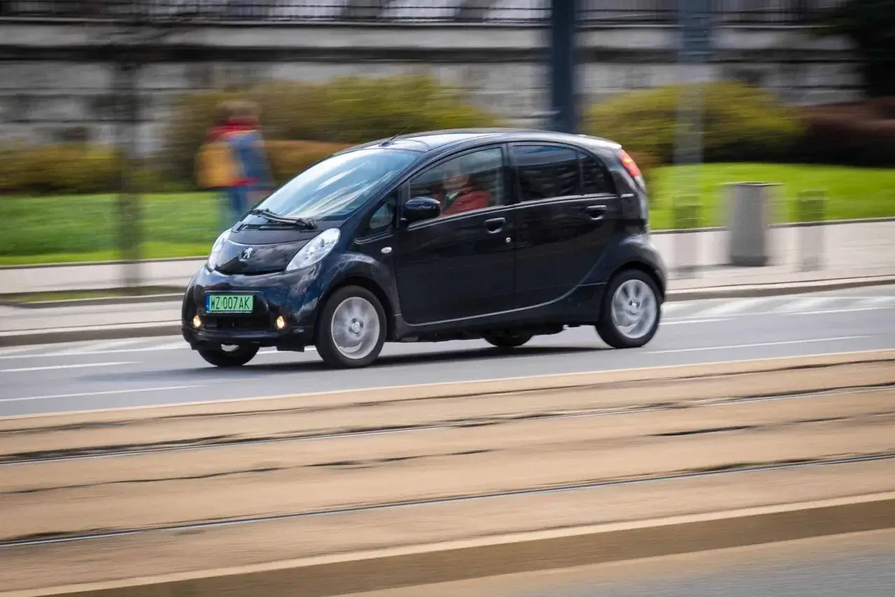 Czarny Peugeot iOn porusza się po ulicy, z rozmytym tłem sugerującym ruch.