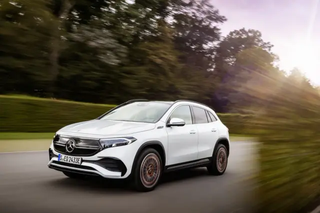 Biały Mercedes EQA 250 pędzi po drodze wśród drzew, tworząc wrażenie ruchu.